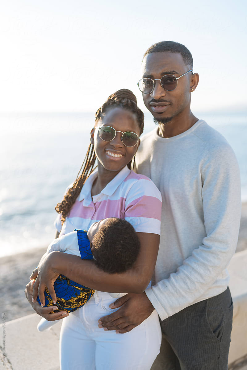 Happy black couple hugging baby and smiling near beach