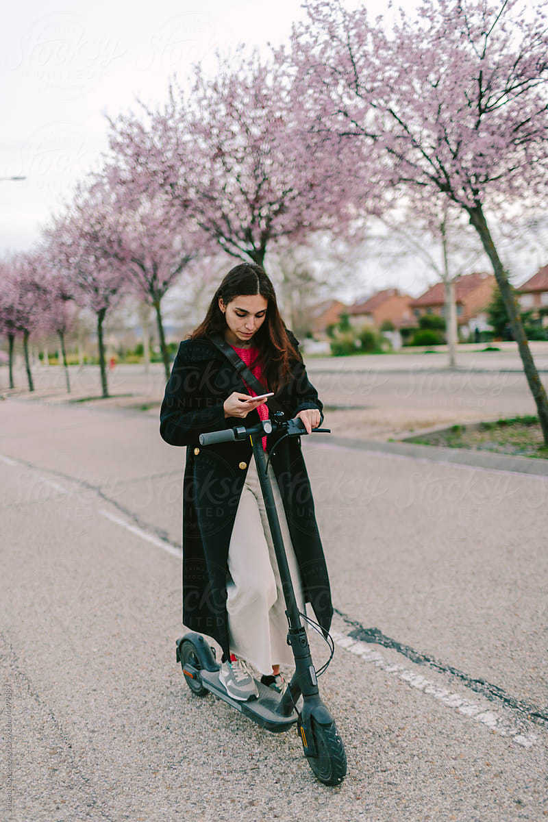 Woman checking smartphone with e-scooter at night in the suburbs