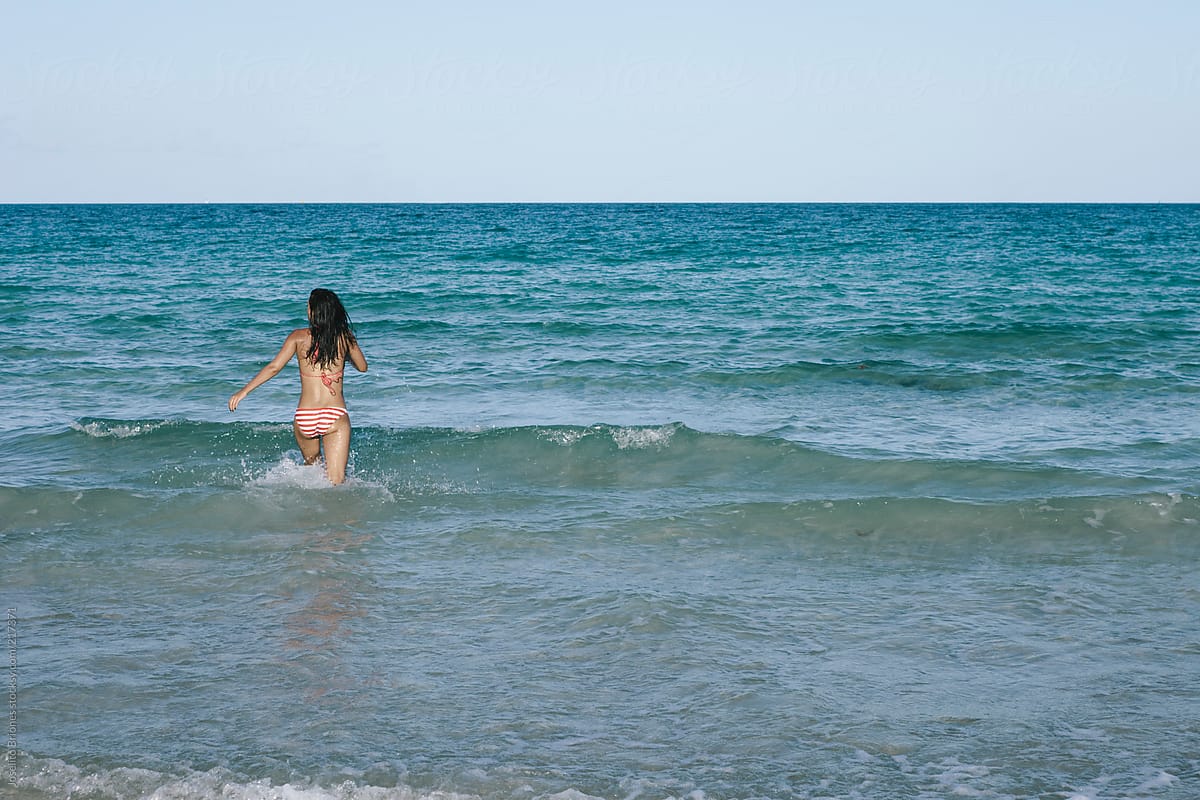 Young Woman In Bikini Wading In Water At The Beach In Summer By