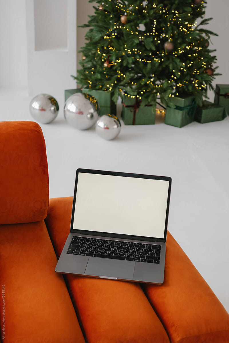 Opened laptop placed against decorated Christmas on sofa at home