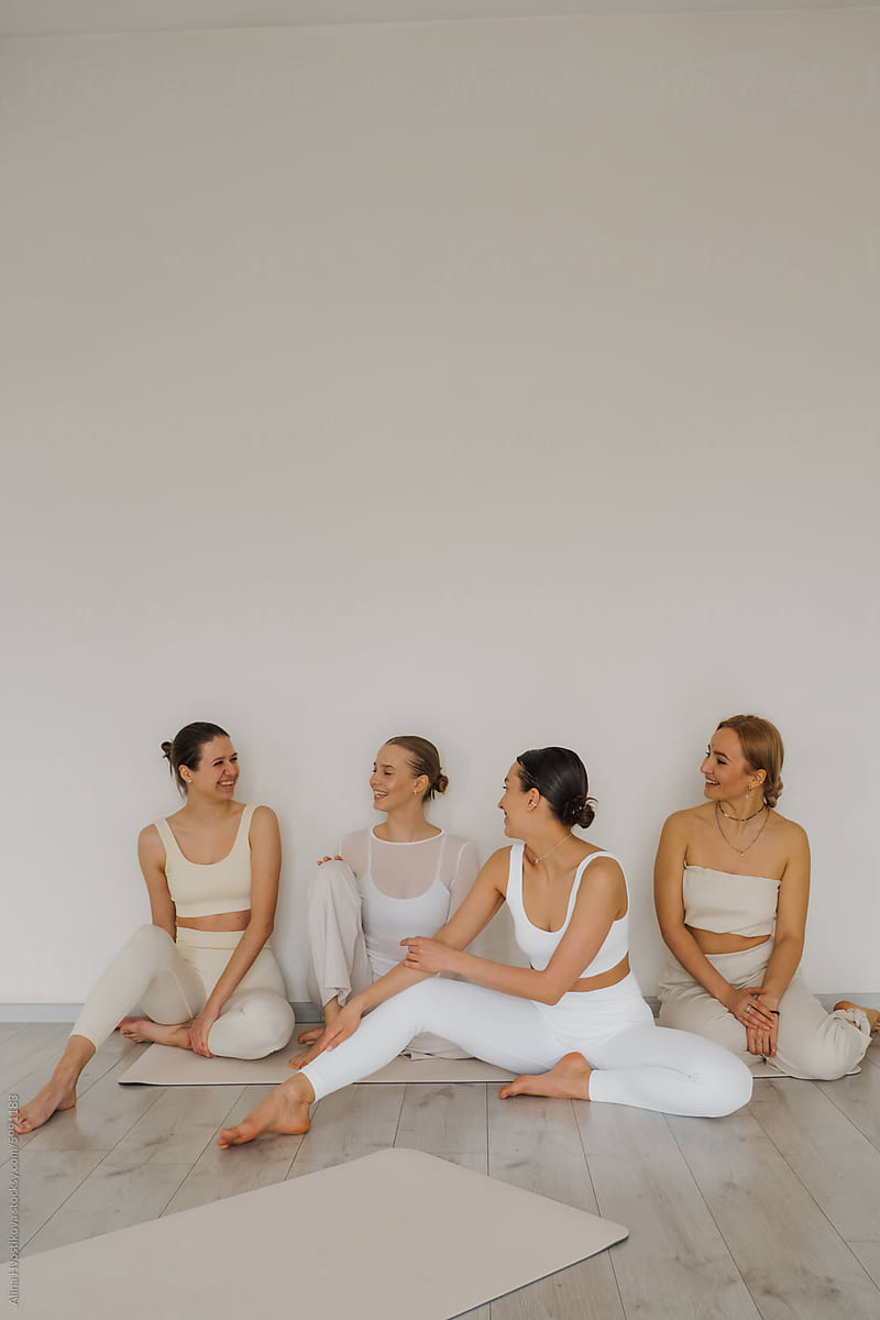 Positive women in sportswear sitting on yoga mat at gym