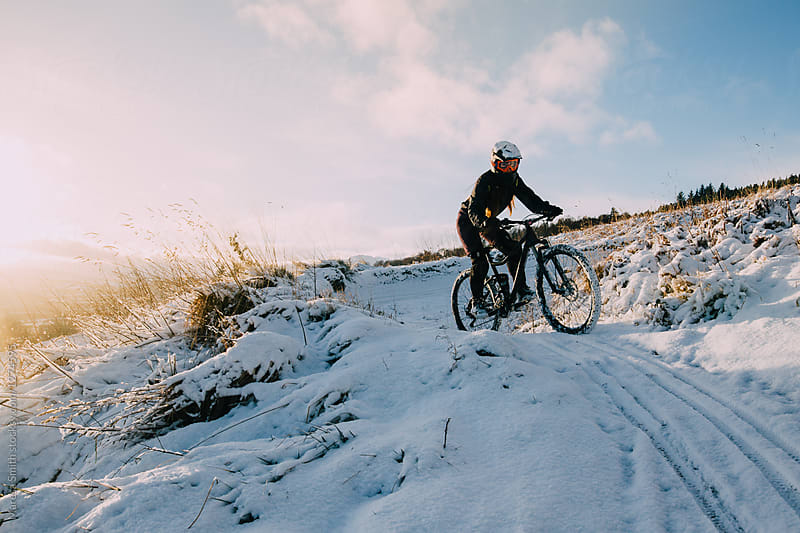 A female mountain biker riding a snowy path coming down a hill at golden hour