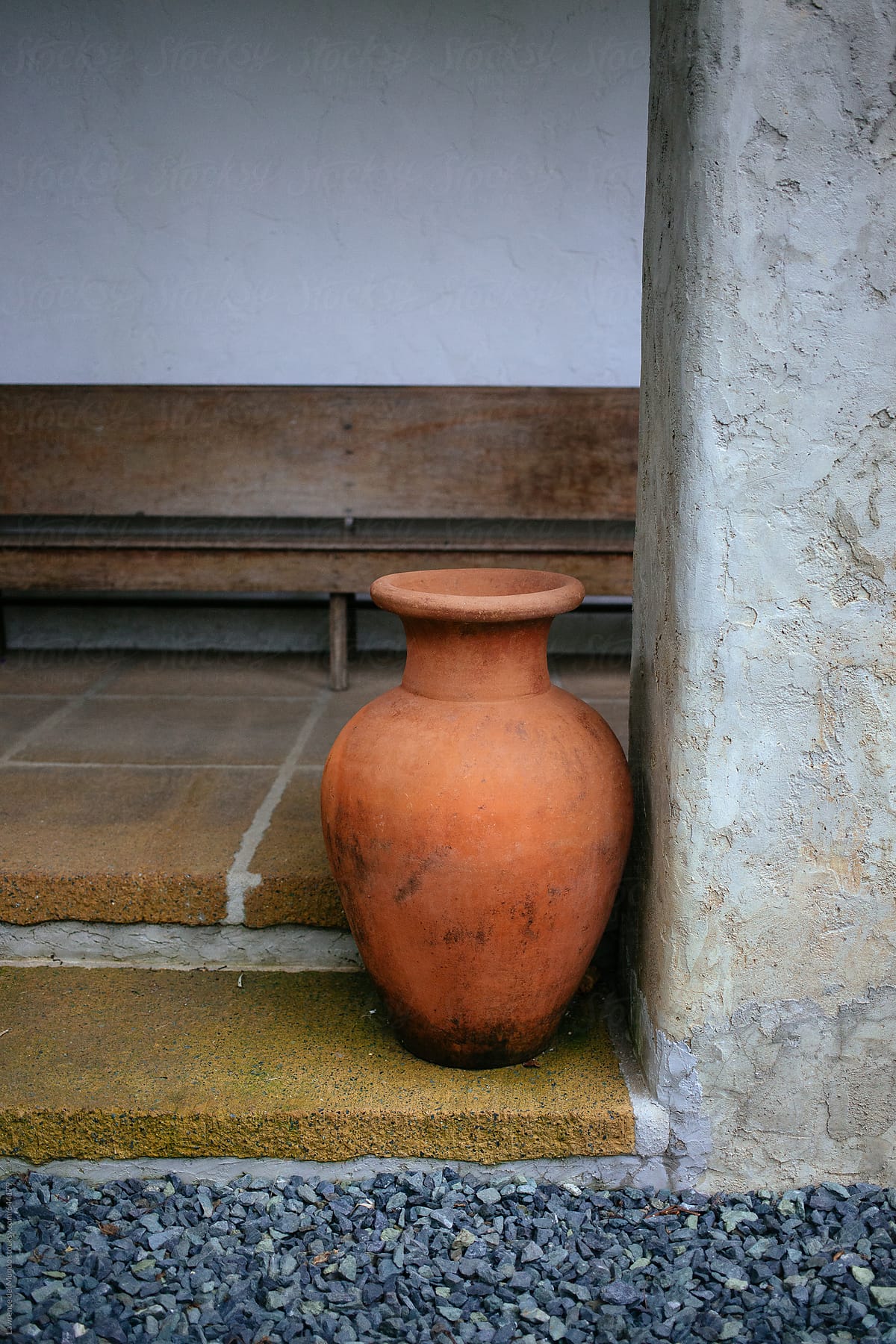 Clay jar beside a gray column with a brown bench in the background