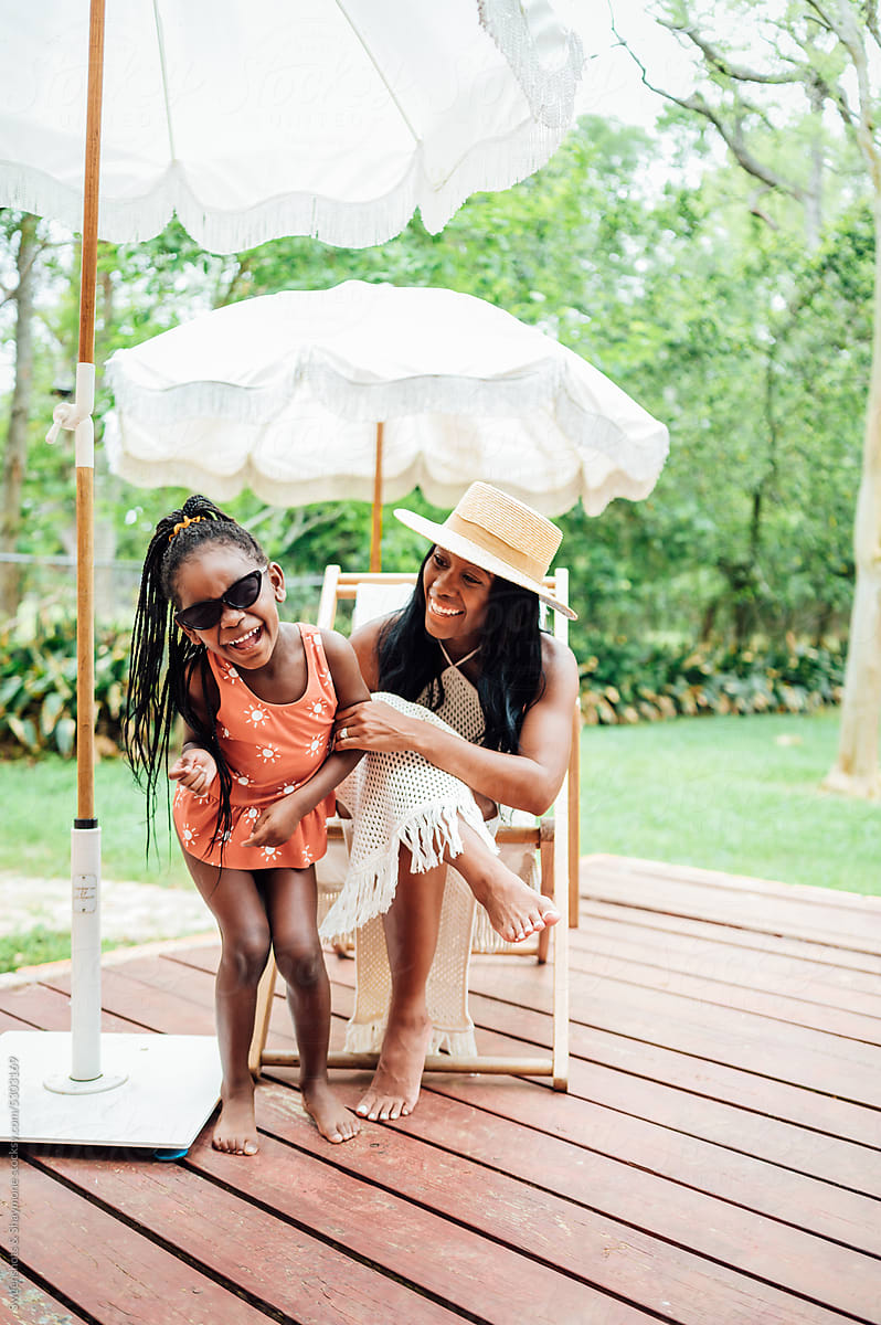 Mom And Daughter Laugh Together Sitting On Deck Under Beach Umbrella By Stocksy Contributor 
