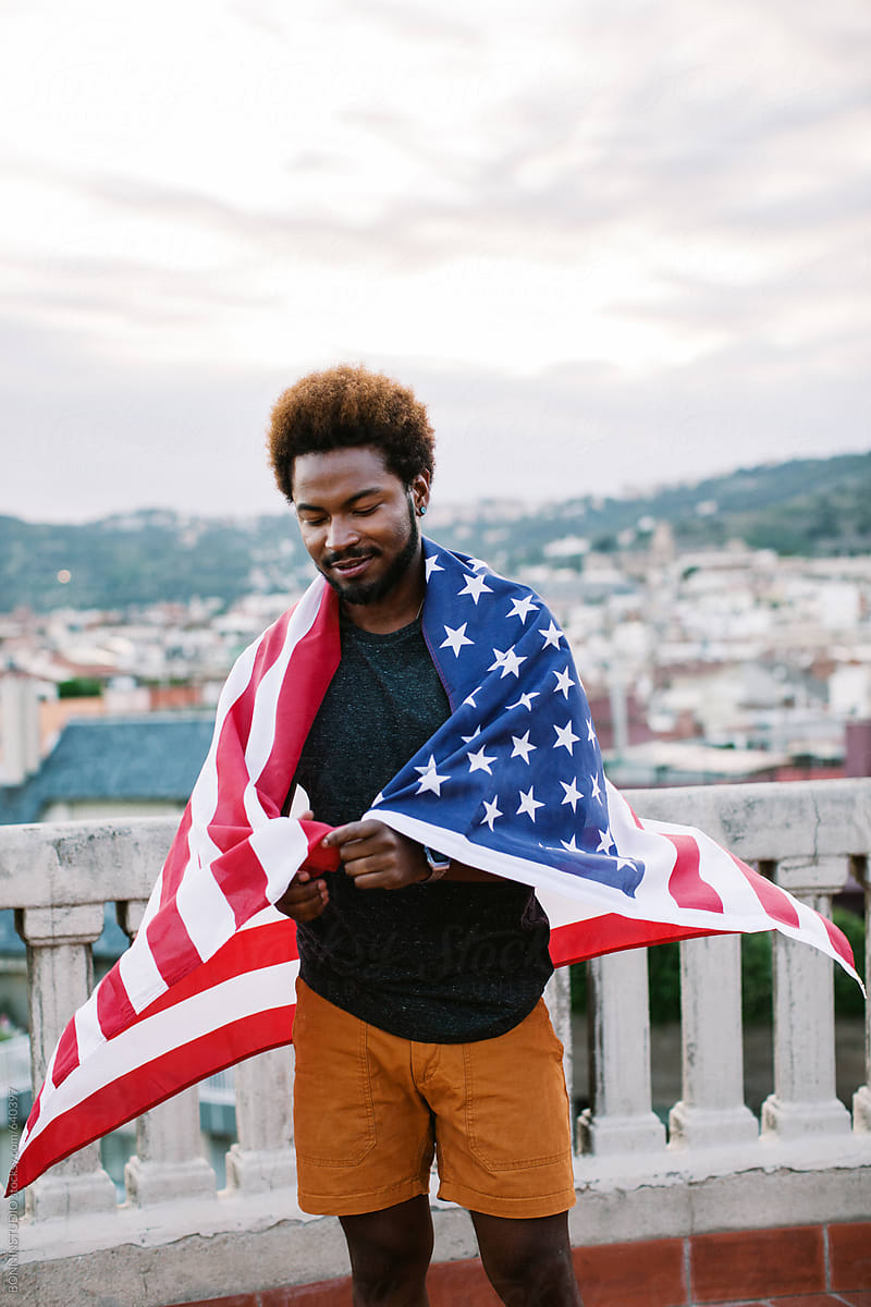 Young black man holding an american flag standing on a rooftop.