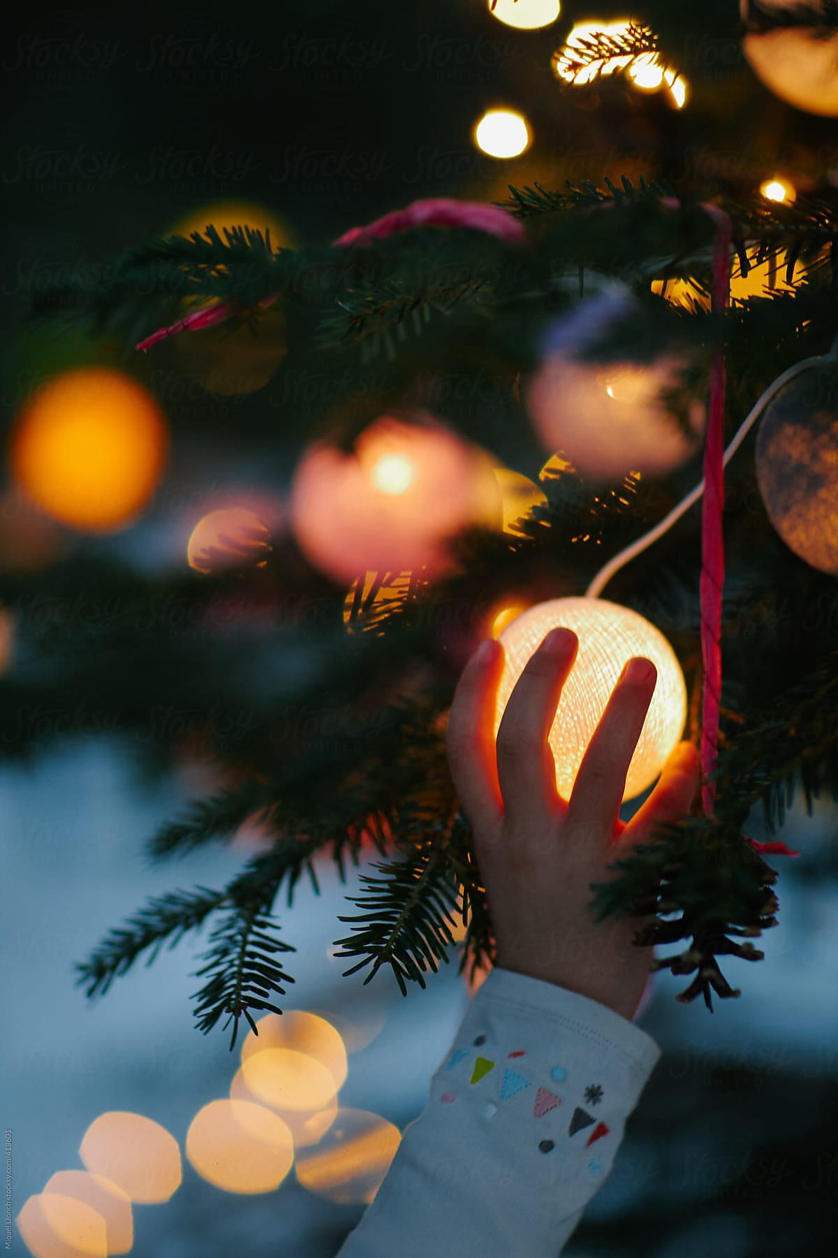 Child hand holding a lit ball at  christmas tree