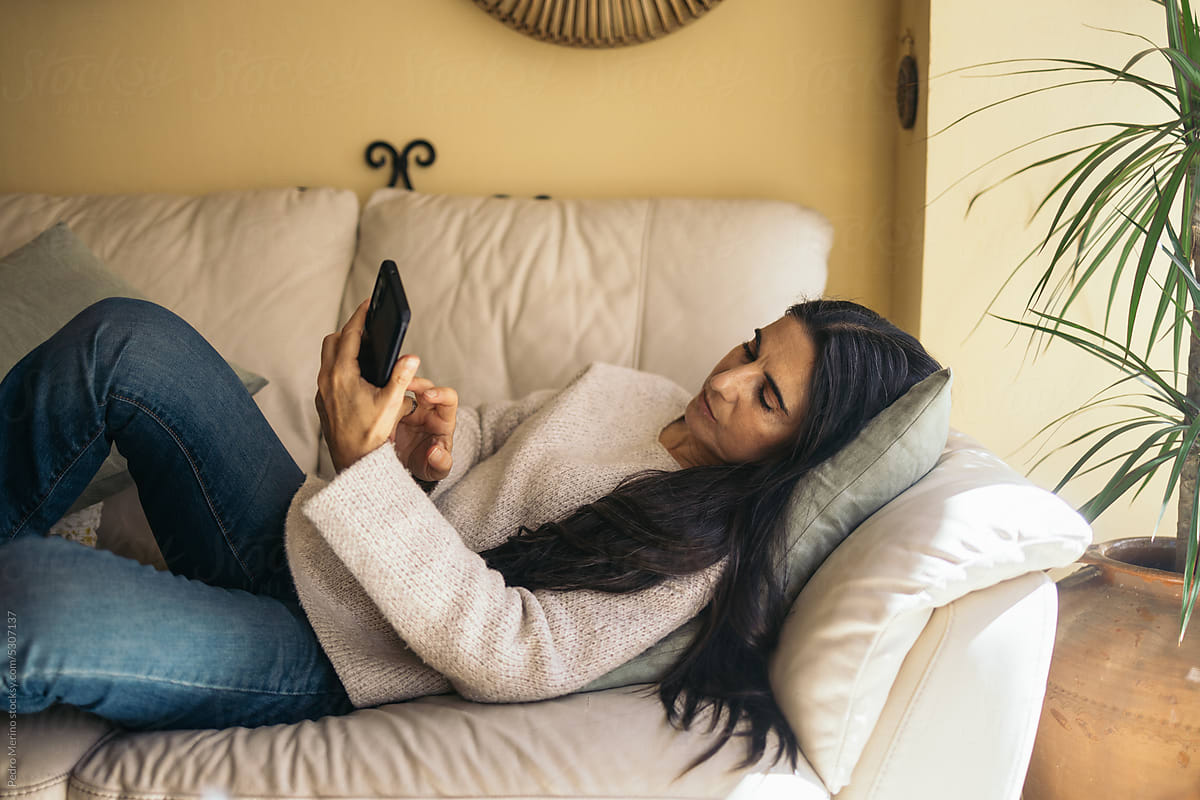 Relaxed woman at home using smartphone lying on sofa