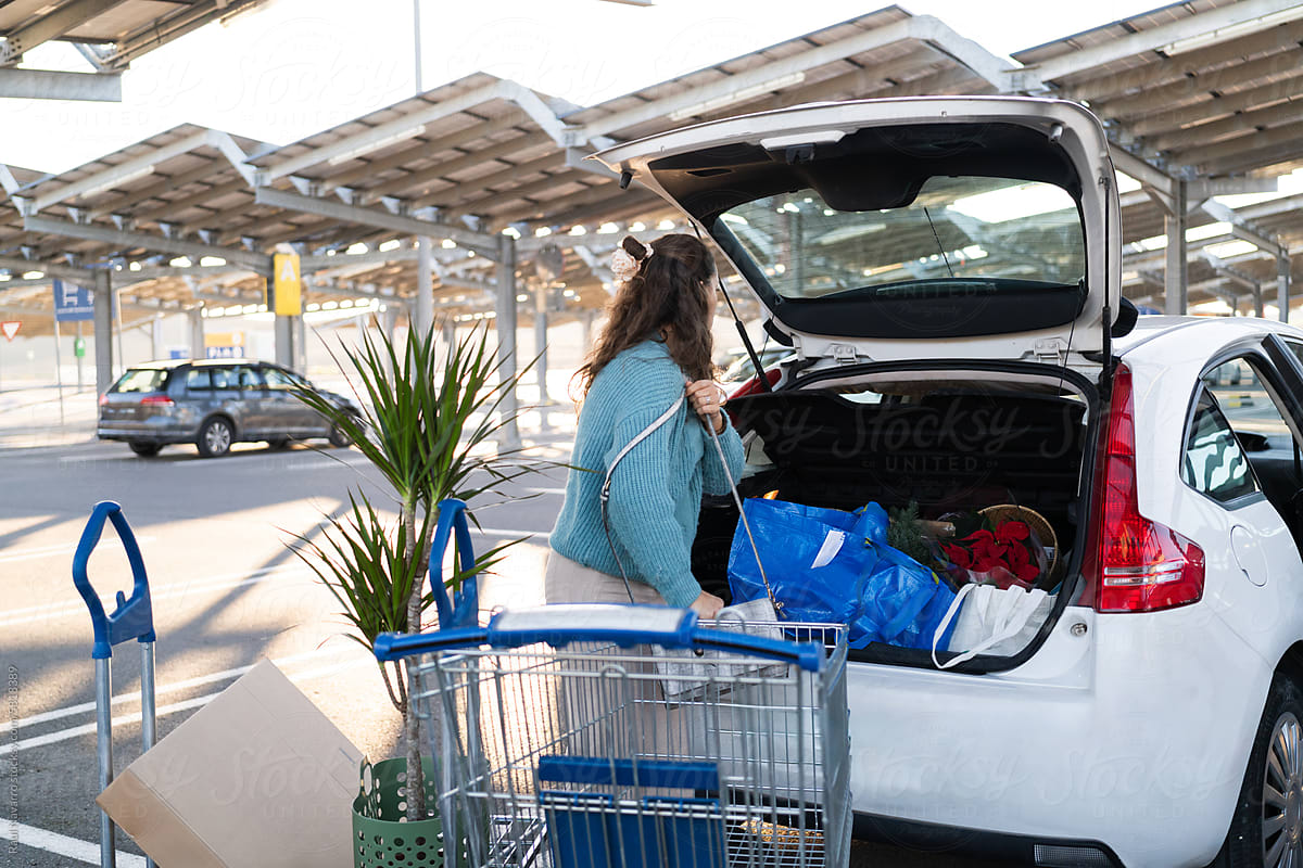 side view of woman  pushing shopping cart with purchases in car trunk