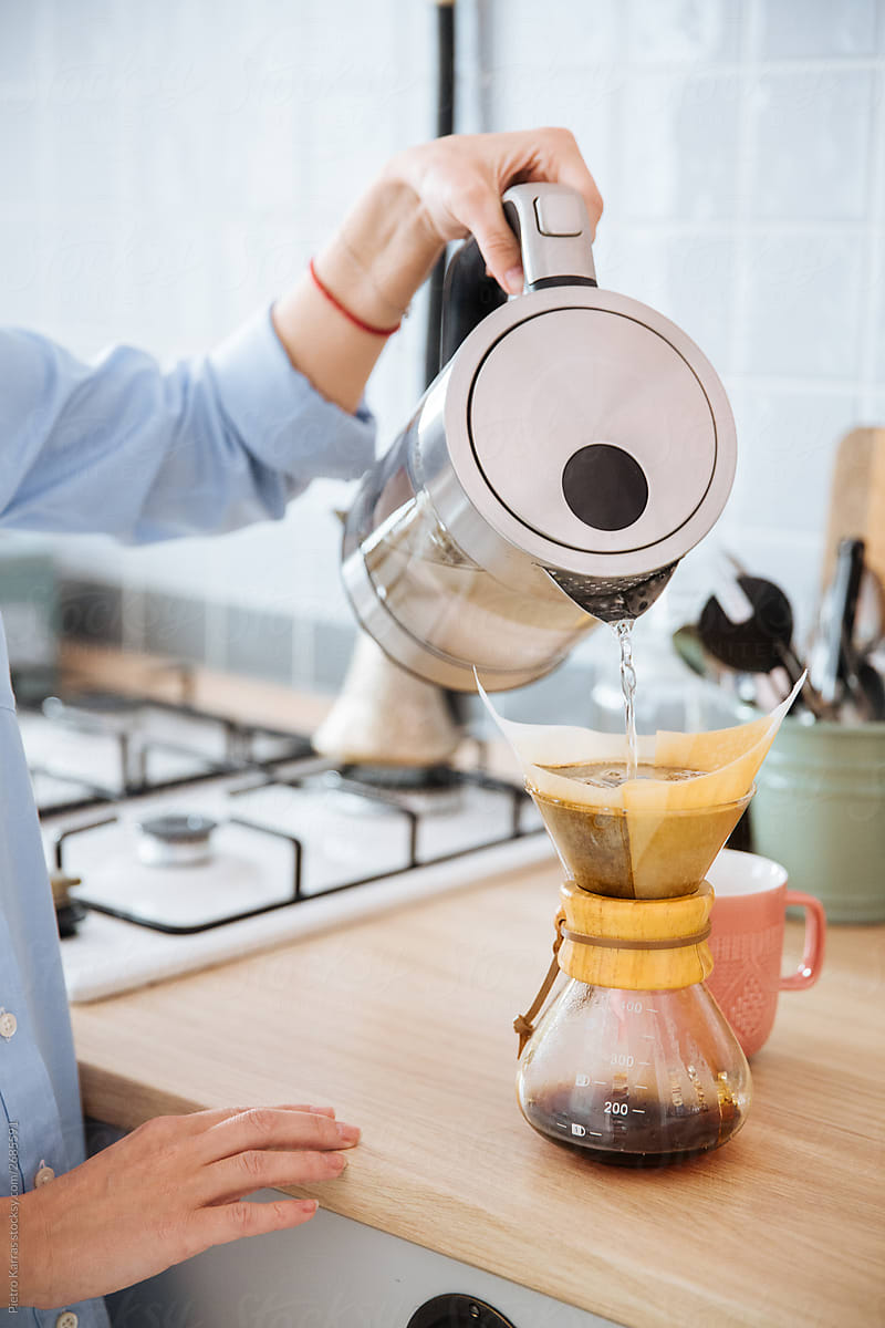 Woman pouring water from kettle in chemex in light kitchen