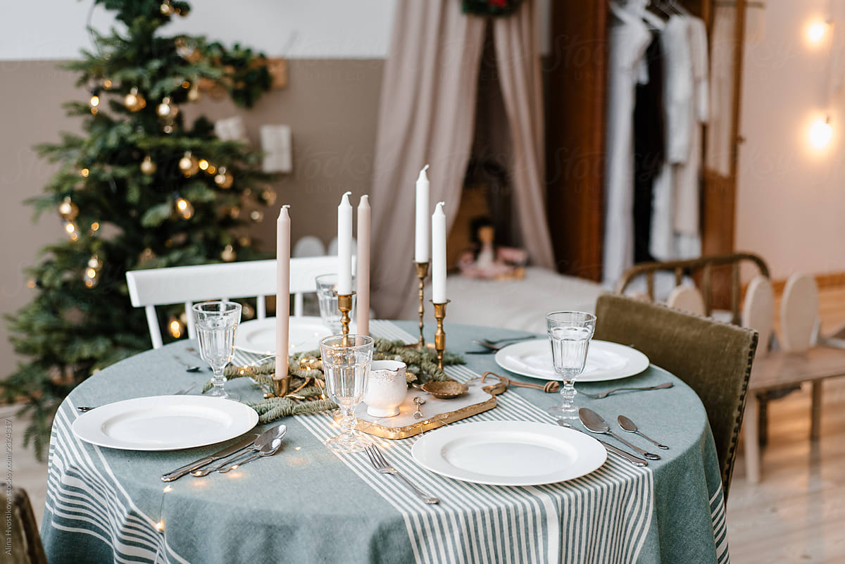 Table served by plates, cutlery and candles near fir tree