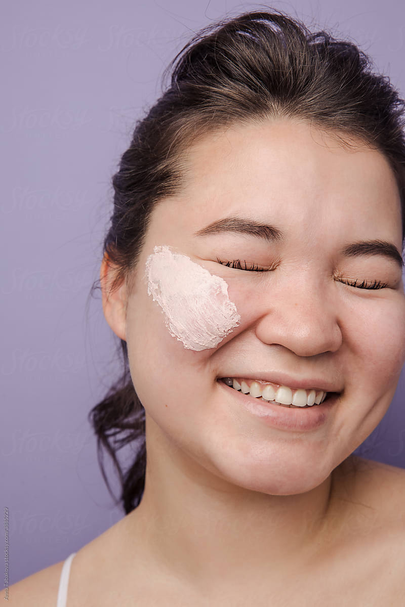 East asian model with pink cream on her face smiling