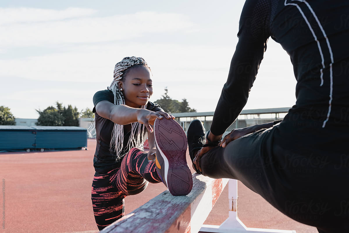 African American sportswoman stretching leg near crop partner