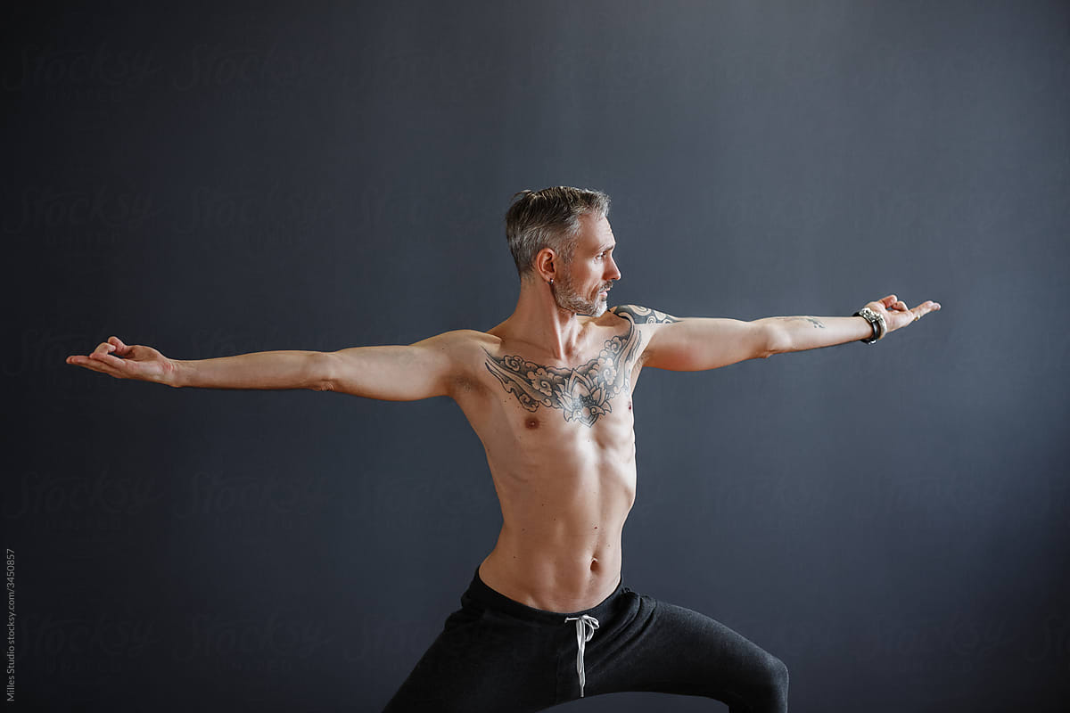 Fit male doing Warrior pose on black background