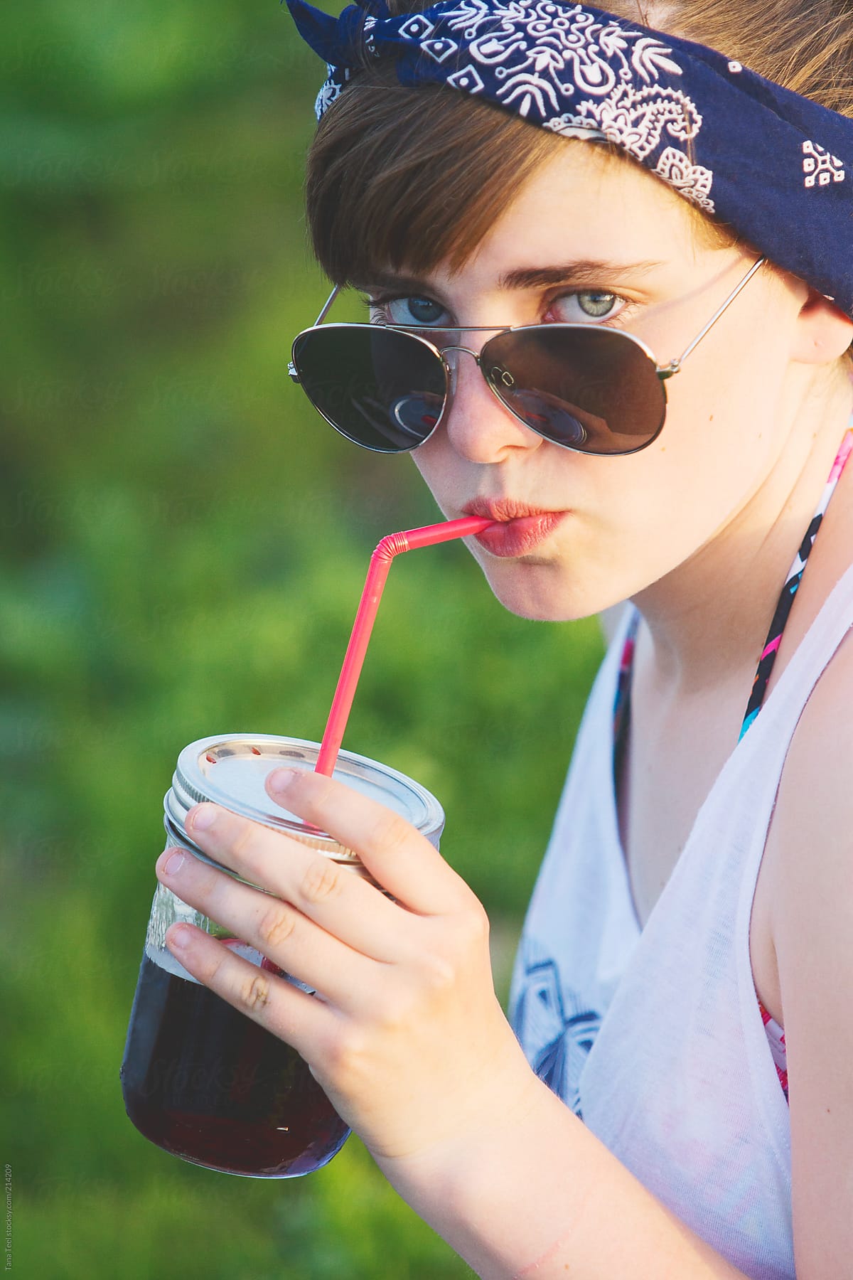 A teen looks over her sunglasses while sipping from a straw