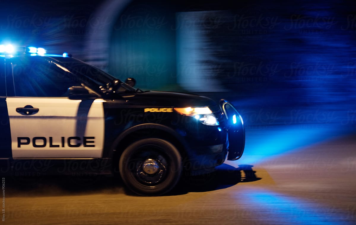 A Police Vehicle Driving Fast With Red And Blue Lights Flashing By Riley