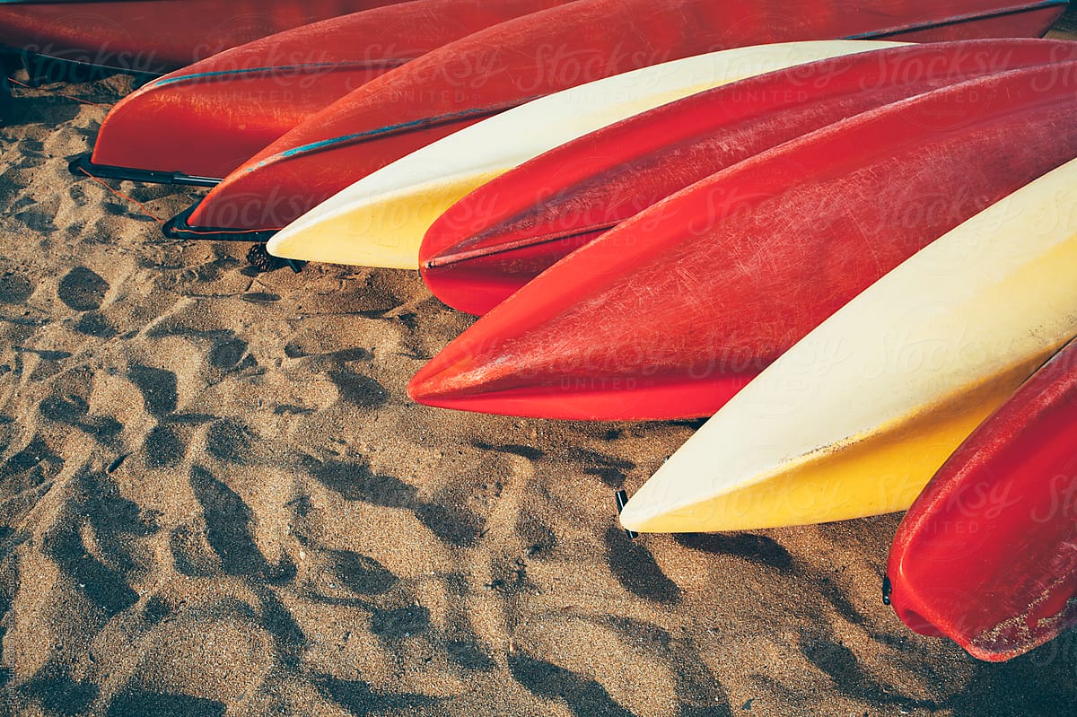 Row of red and yellow plastic rental canoes on beach
