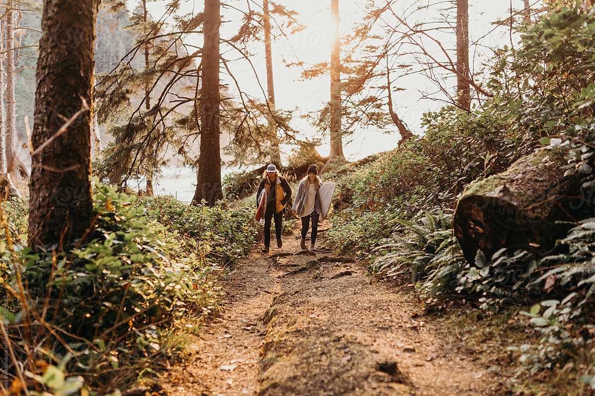 Couple hiking on a forest trail with surfboards