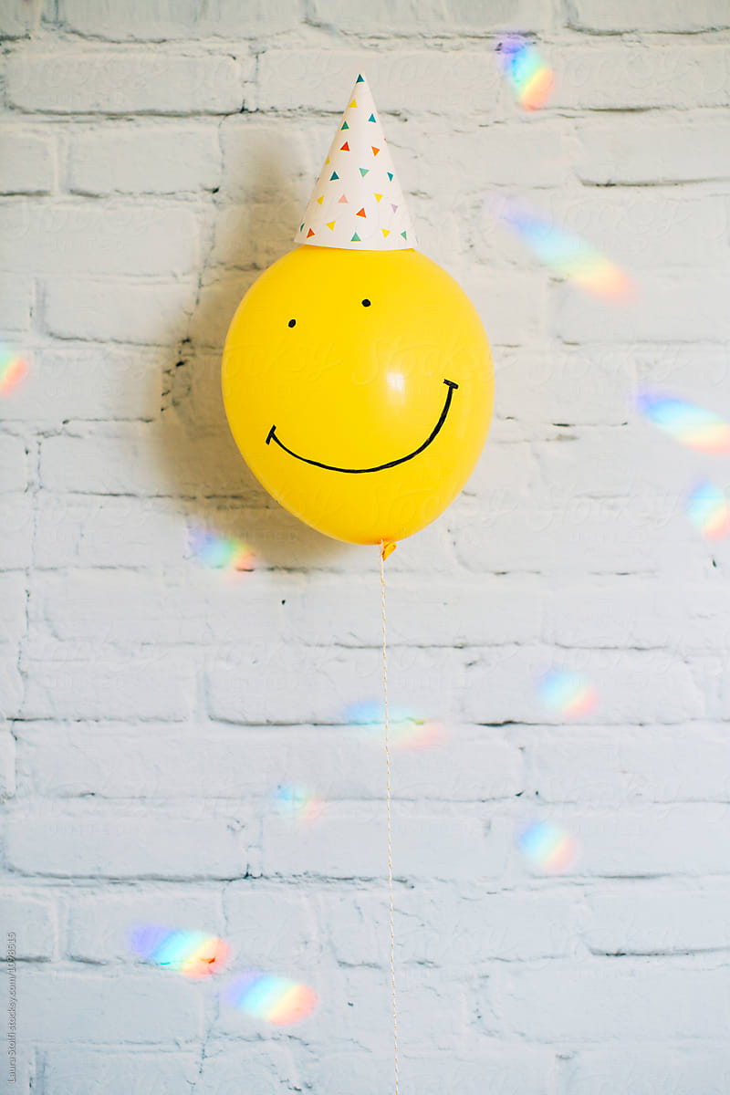 Many rainbow lights around yellow balloon with smiling face and party hat