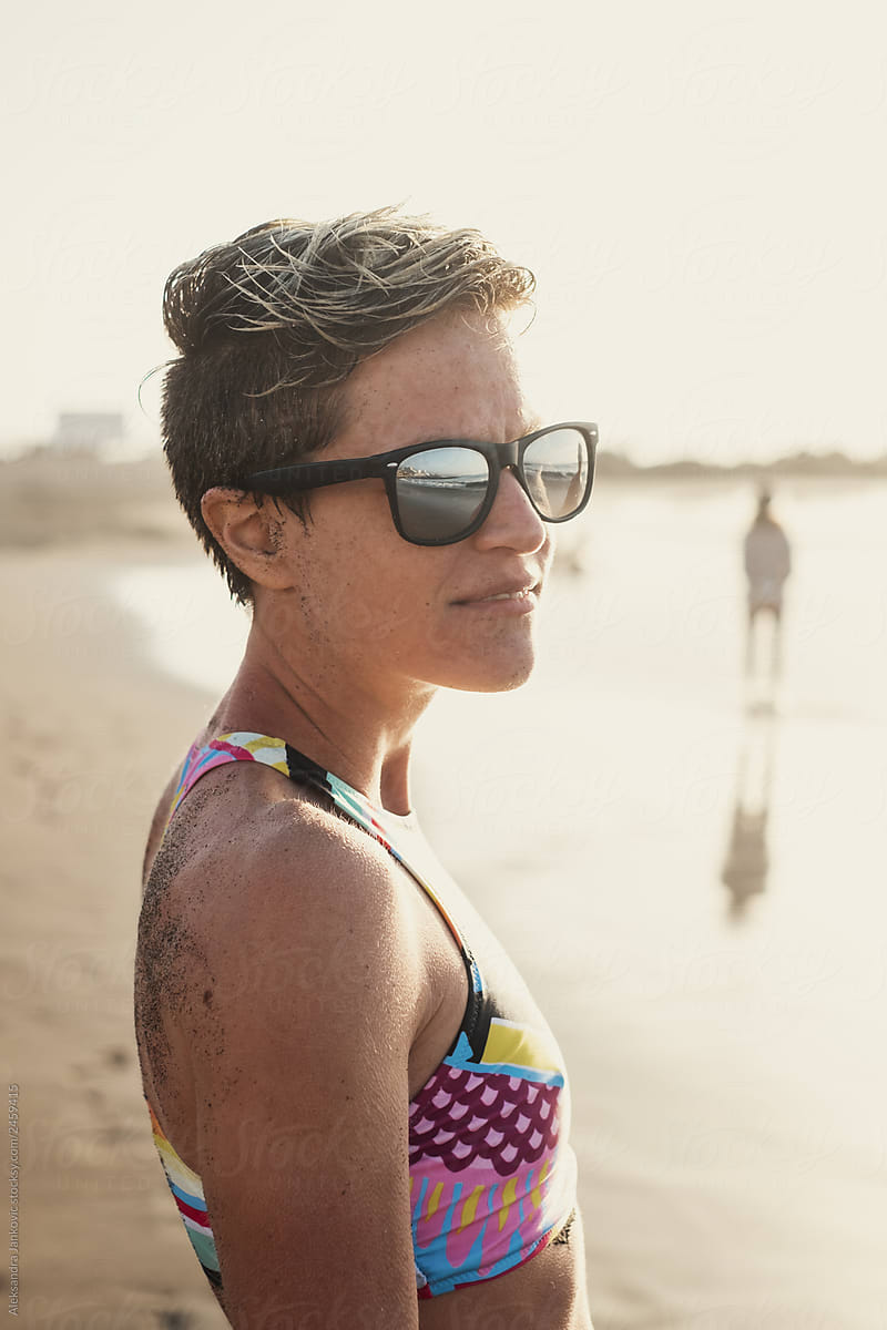 Smiling Short Haired Woman Wearing Sunglasses At The Beach Del Colaborador De Stocksy