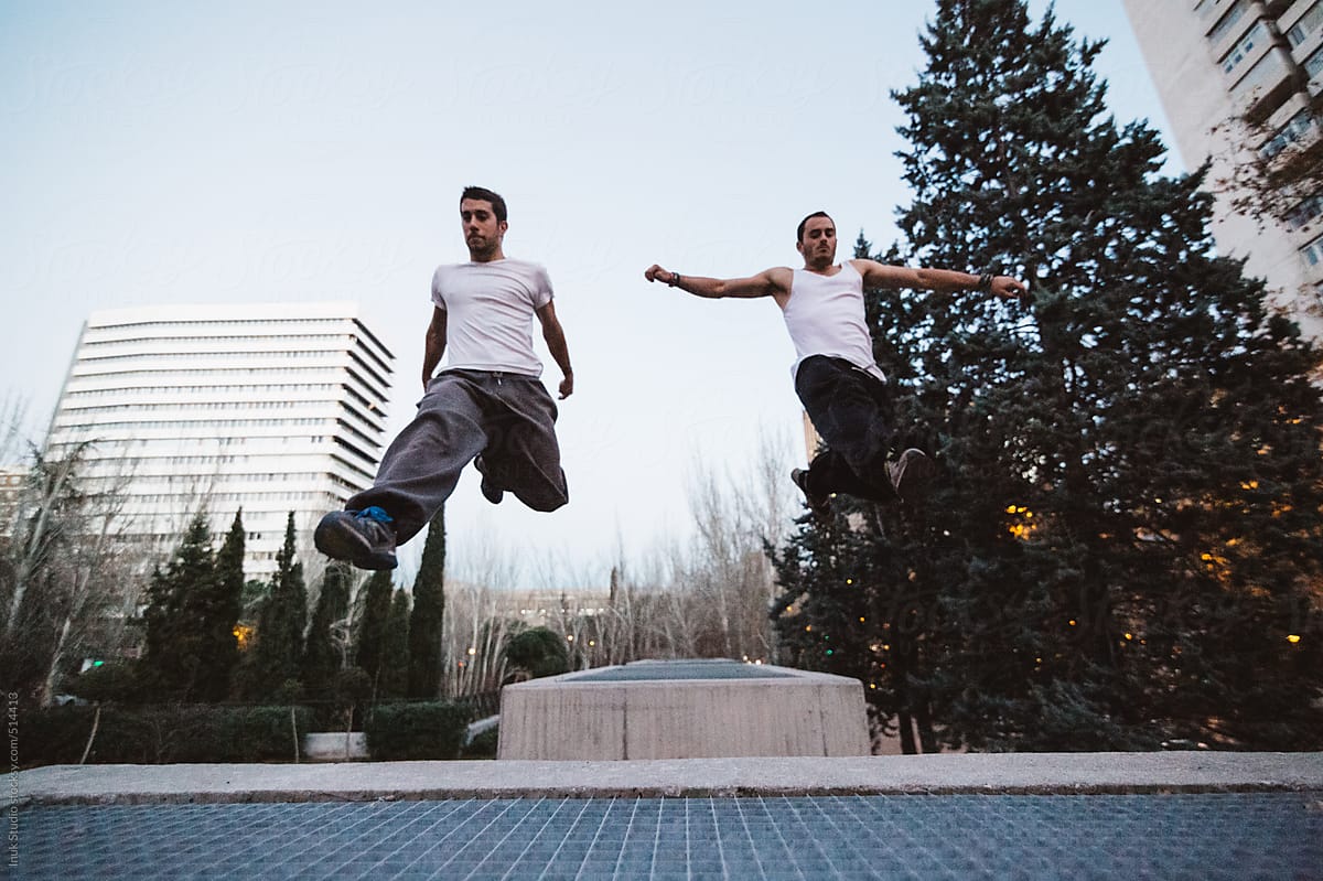 Two men jumping during a parkour training at sunset
