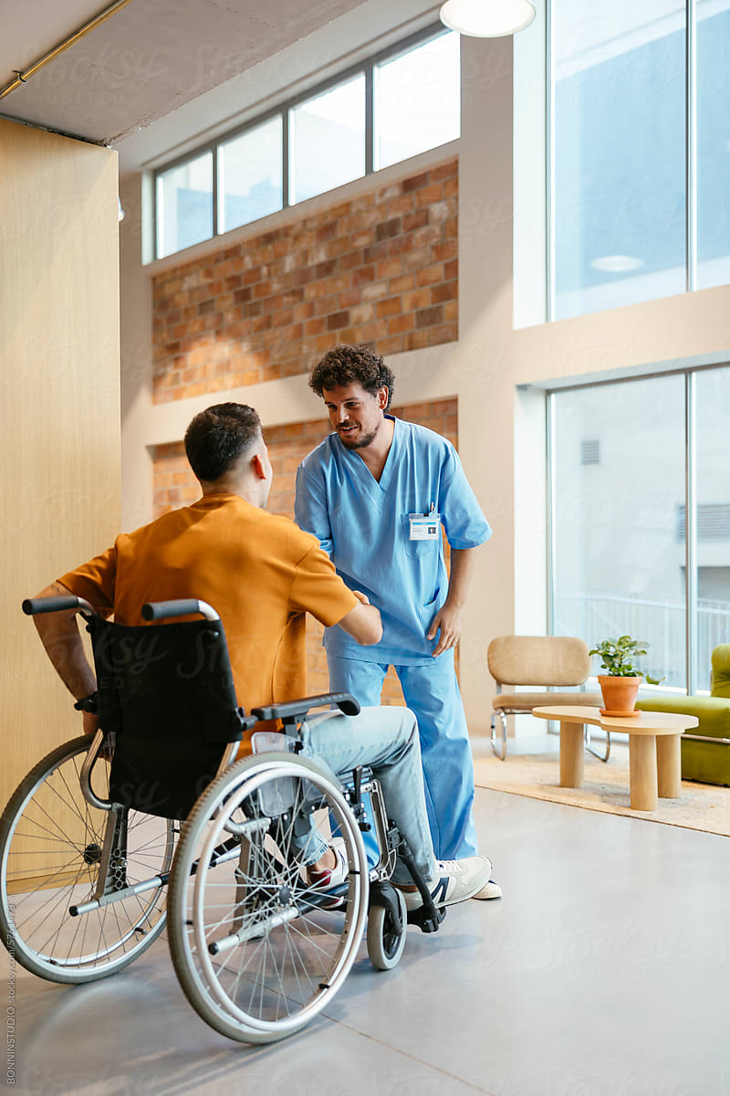 Male nurse and man in wheelchair greeting each other at hospital