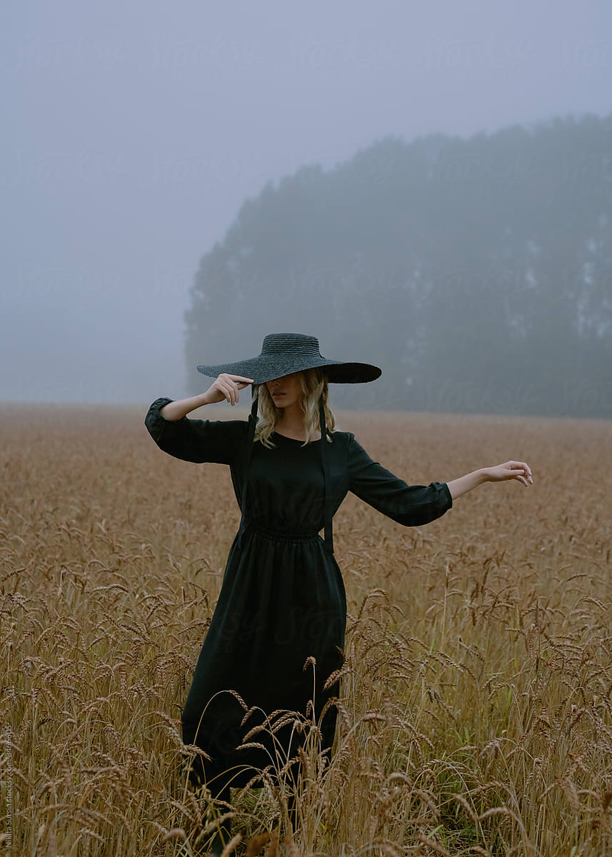 girl in a hat and black dress posing in a wheat field