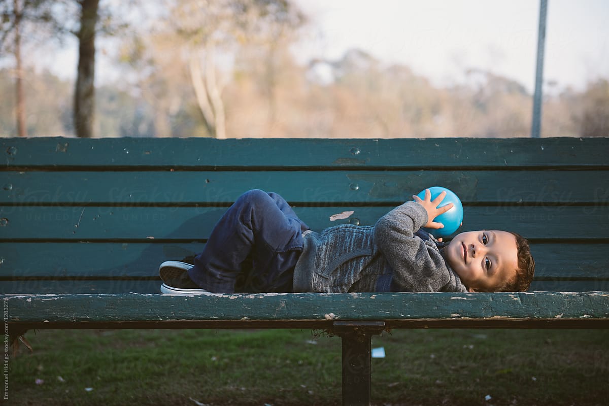Boy lying down on park bench holding his ball