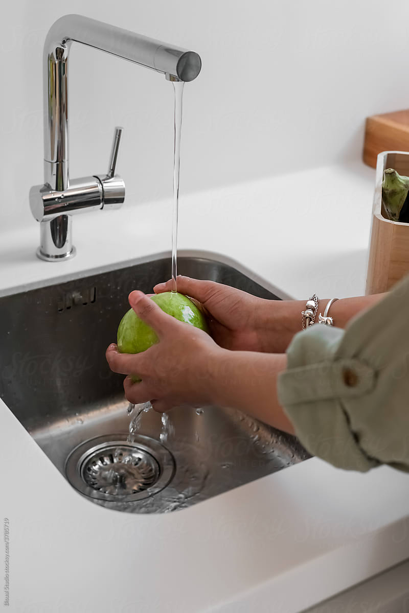 Housewife washing fruit under tap in kitchen
