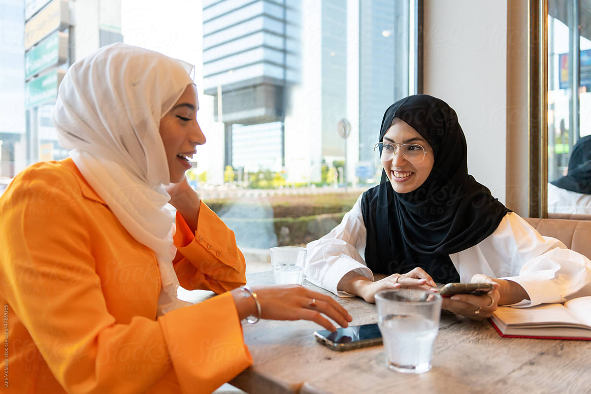 Two Muslim Girls Talking In A Urban Cafe.