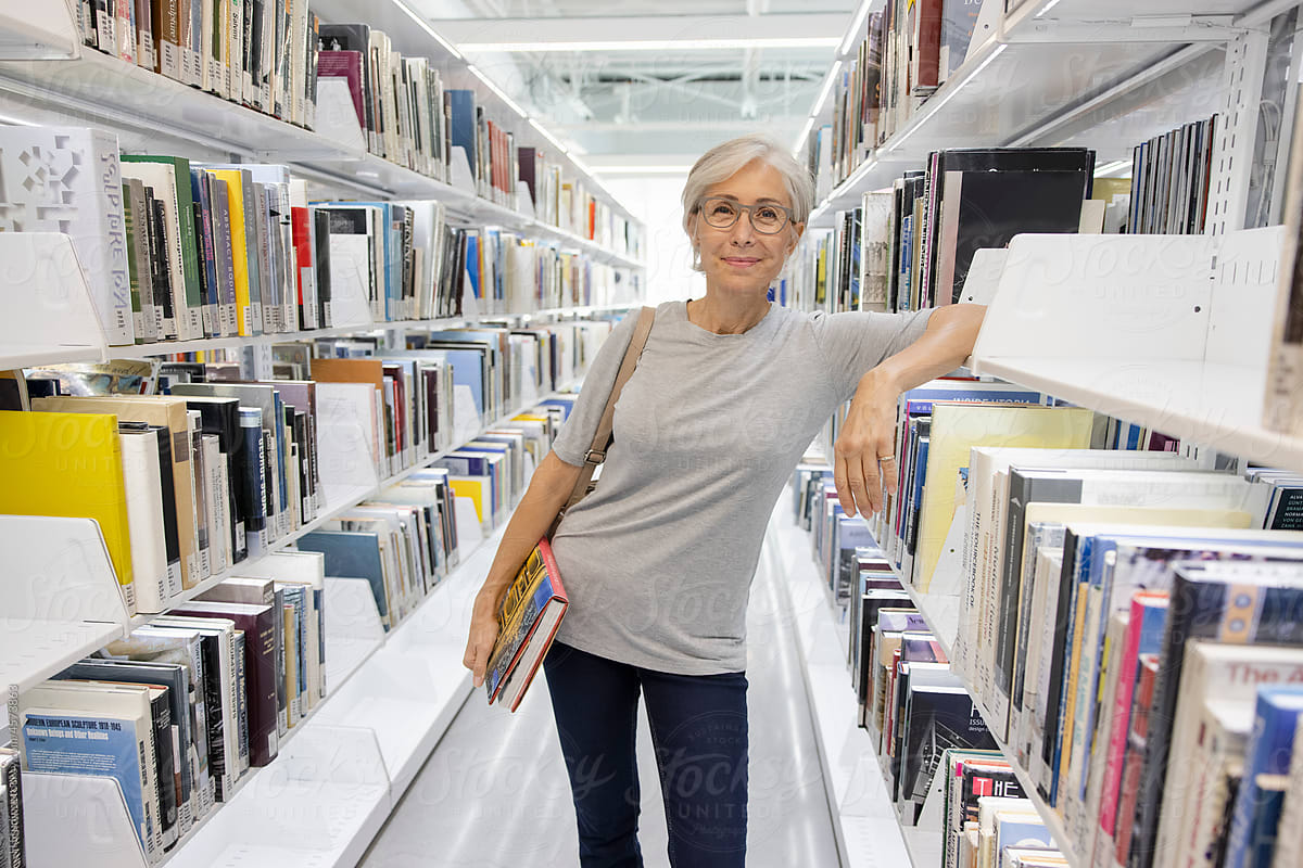 Portrait confident senior woman at bookshelf in library.