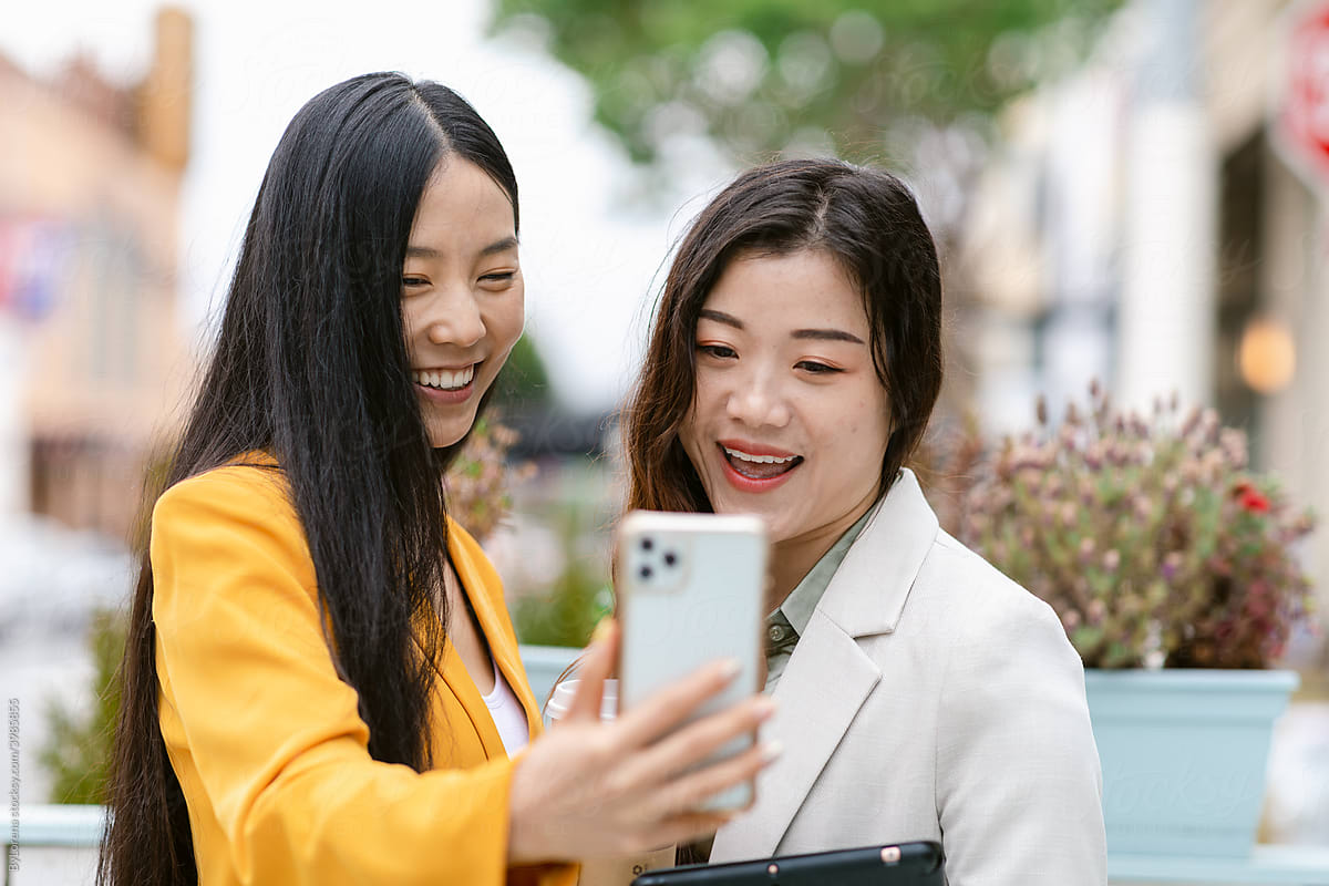 Cheerful Chinese girlfriends making video call on street