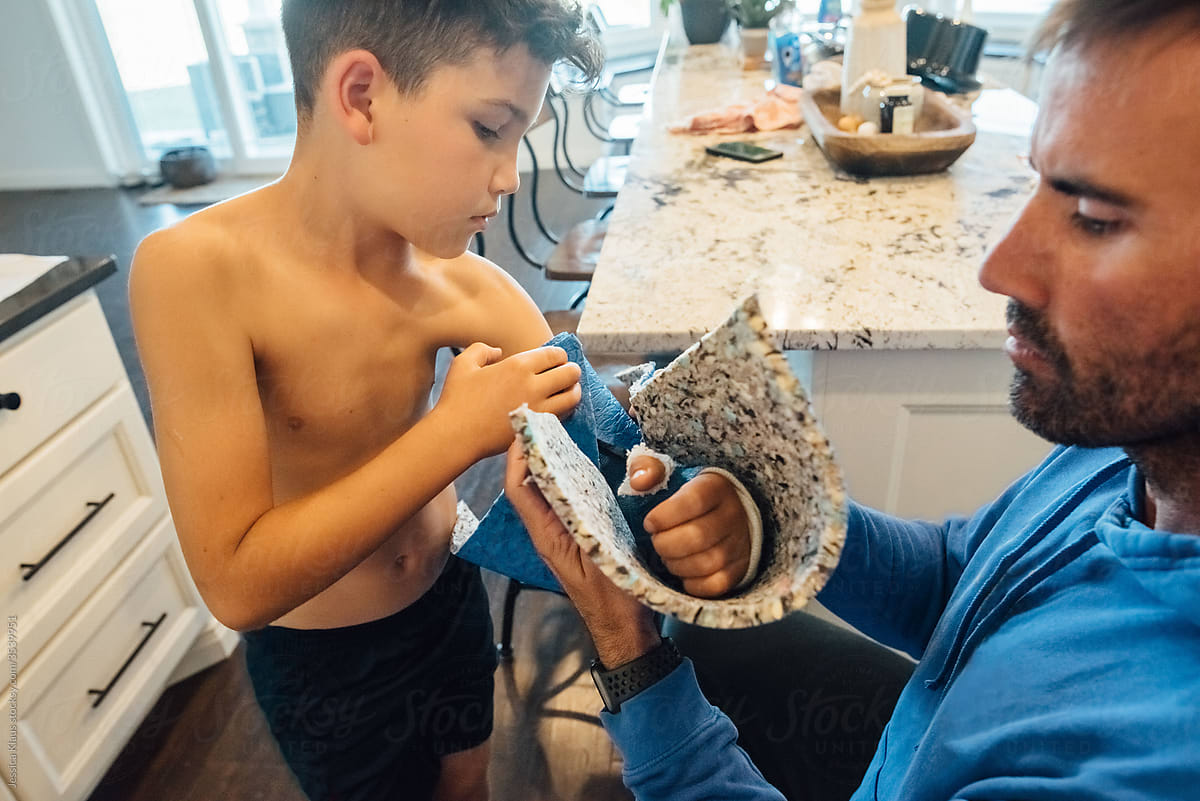 Father making a protective covering for son\'s casted arm.