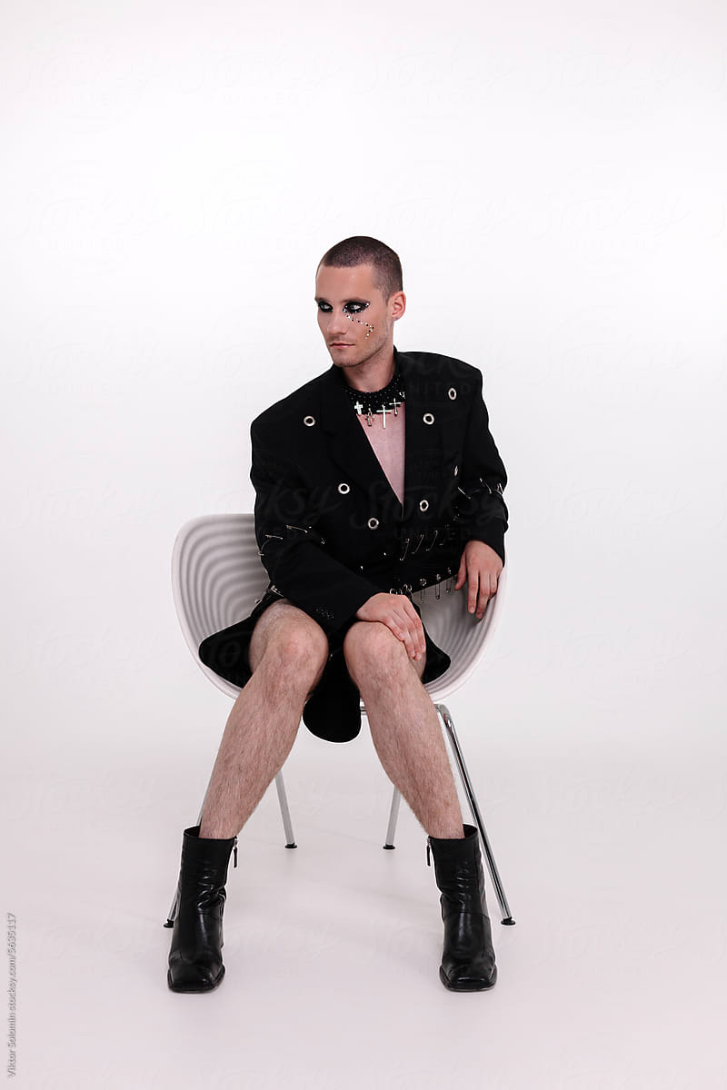 Stylish androgynous man in suit sitting on chair and looking at camera