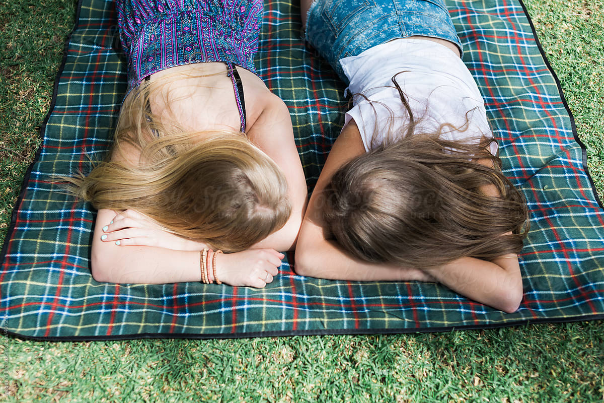 Looking Down On Two Teenage Girls Lying Face Down On A Picnic Rug By