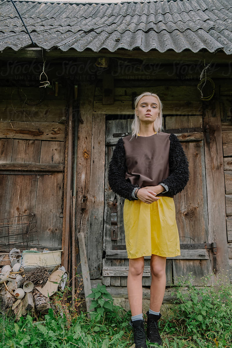 beautiful and stylish girl in a yellow retro dress, standing near the barn in the village