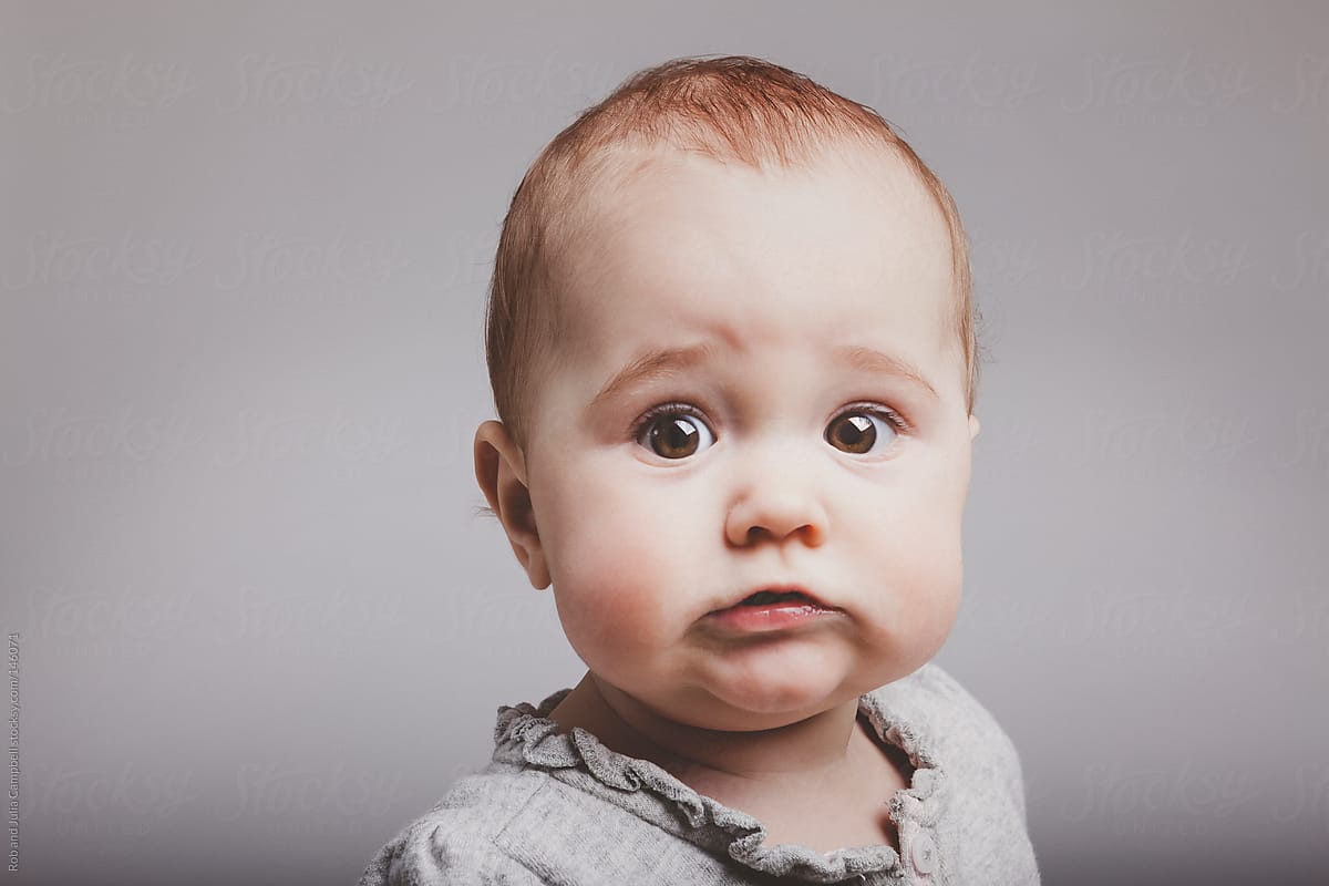 Cute baby girl with funny face on solid background
